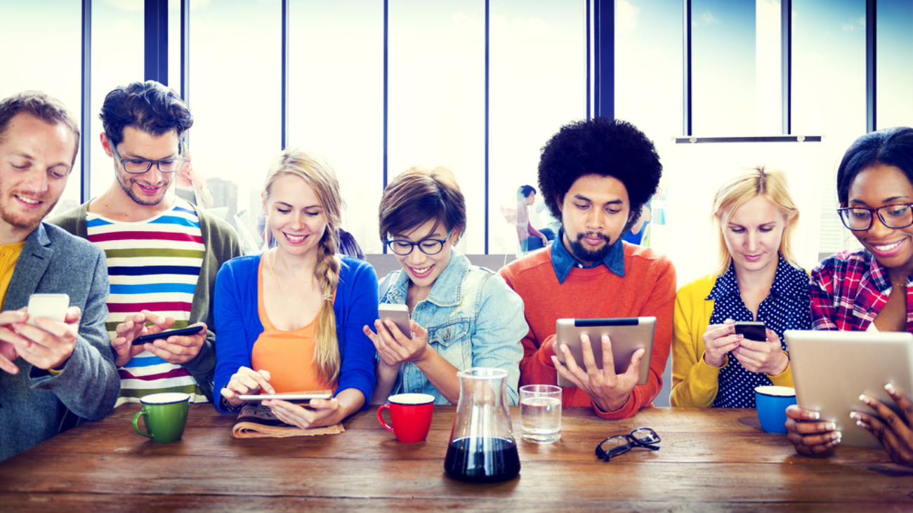 Image of young people around a table using mobile devices